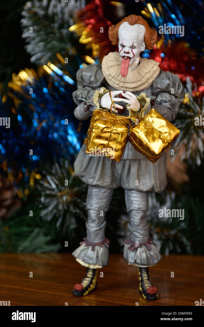 Action figure della NECA del clown Pennywise tratto dal film horror IT. Giocattolo con la linguetta appesa, vista ravvicinata. Scatole regalo luminose in miniatura, albero di Natale. Foto Stock