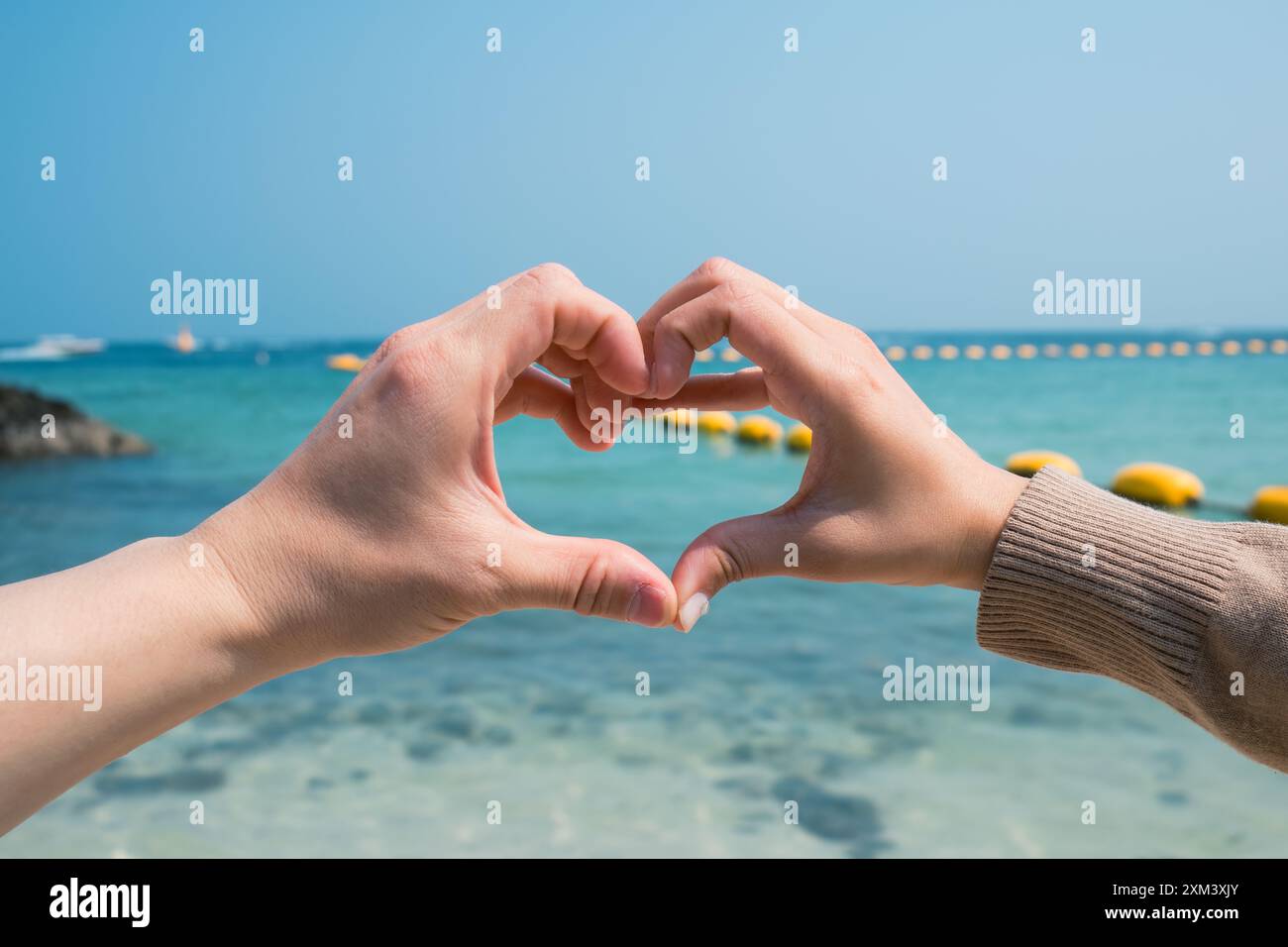 Accoppiare due mani che si formano e fanno un gesto a forma di cuore sulla spiaggia. Concetto di amore e affetto Foto Stock