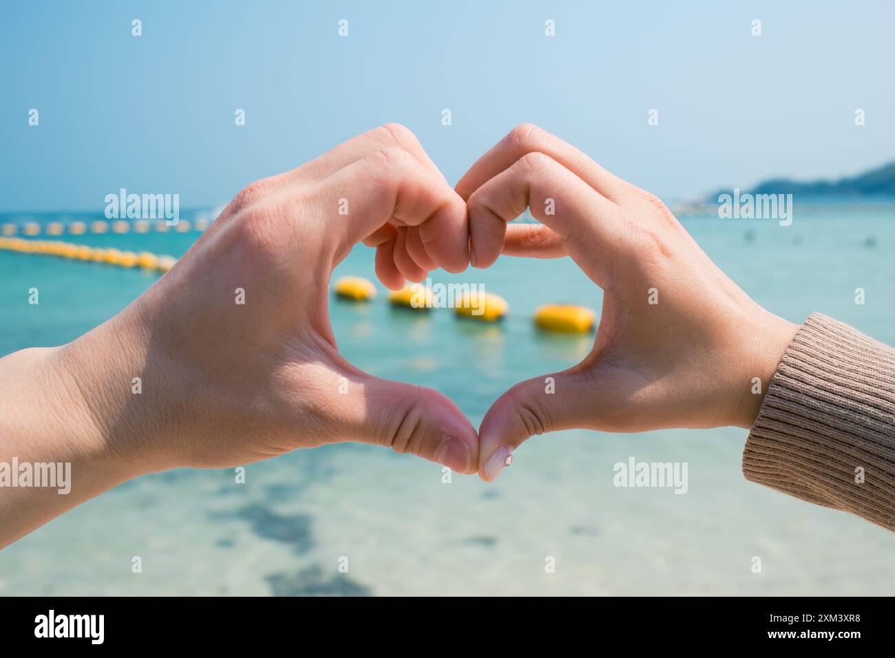 Accoppiare due mani che si formano e fanno un gesto a forma di cuore sulla spiaggia. Concetto di amore e affetto Foto Stock