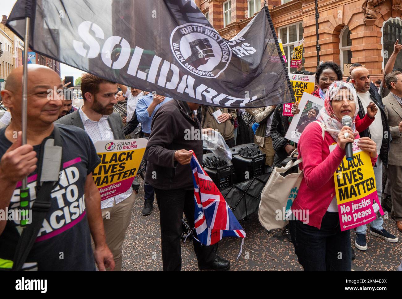 Nahella Ashraf di "Stand Up to Racism" (sciarpa da testa) guida la protesta. Greater Manchester Stand Up to Racism (GMSUTR) ha organizzato una protesta oggi presso gli uffici del sindaco della Greater Manchester Combined Authority (GMCA) Andy Burnham su Oxford Street nella città di Manchester. I manifestanti hanno chiesto la fine immediata della violenza razzista della polizia da parte della Greater Manchester Police (GMP) a seguito di un video di recente diffusione catturato martedì sera al Terminal 2 dell’aeroporto di Manchester. Il filmato cattura un ufficiale che prende a calci in faccia un membro del pubblico seguito dall'ufficiale che timbra l'individuo Foto Stock