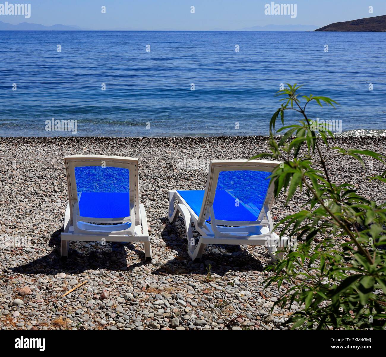 Sedie a sdraio sulla spiaggia rocciosa di fronte al mare a Livadia, Tilos Island, Dodecaneso, Grecia, UE. Presa nel giugno 2024 Foto Stock