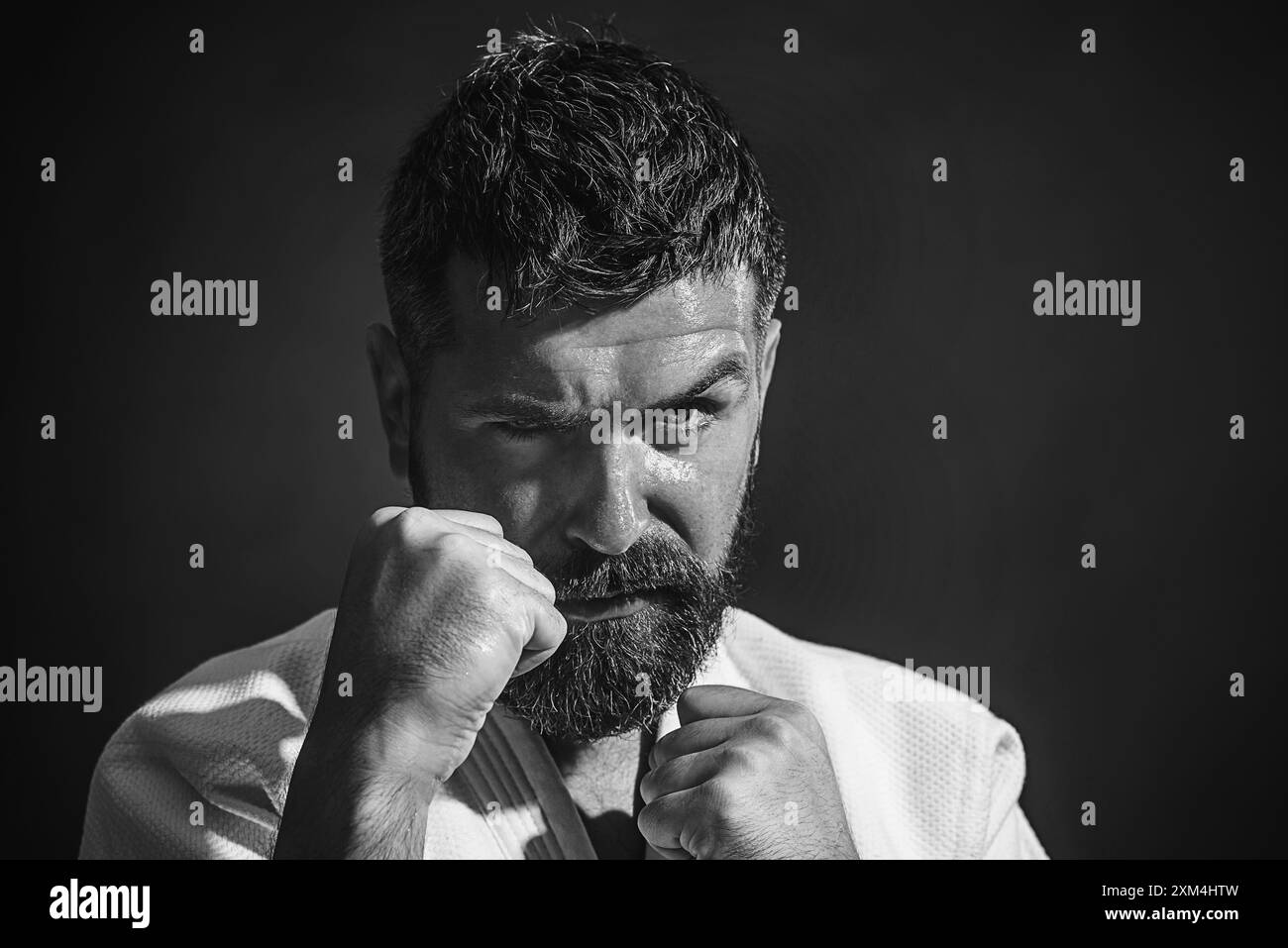 Uomo di karate in posizione di combattimento. Uomo di karate barbuto in kimono bianco per sambo, judo, jujitsu con le mani schiacciate in pugni pronti a combattere. Misto marziale Foto Stock