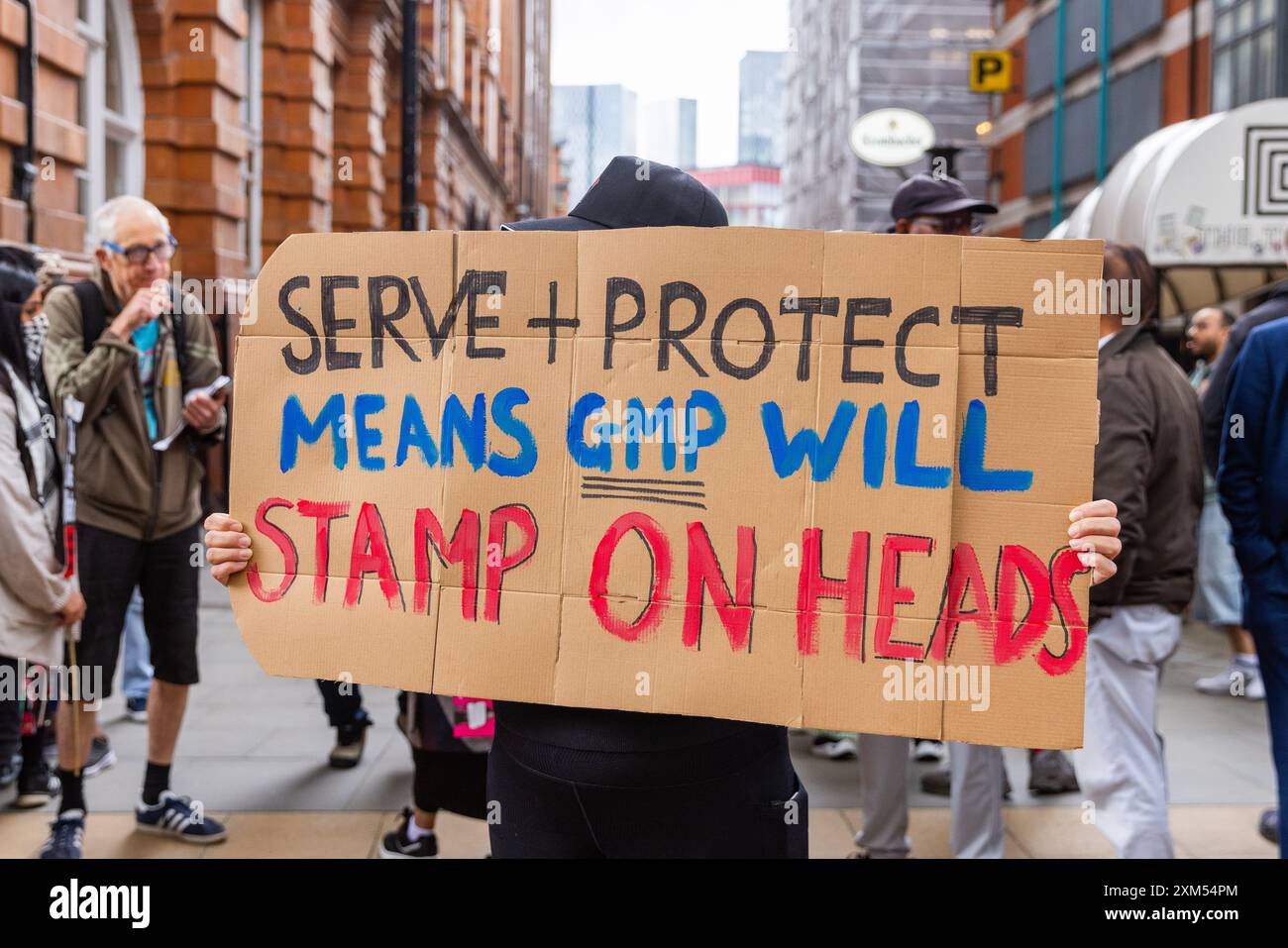Manchester, Regno Unito. 25 LUGLIO 2024. L'attivista ha un cartello "serve + Protect Means GMP stamp on heads", mentre i manifestanti si sono riuniti in una dimostrazione contro un video rilasciato dall'aeroporto di Manchester in cui gli ufficiali di armi da fuoco GMP sono stati visti usare la forza contro i manifestanti con l'incidente rinviato all'IPCC. I manifestanti bloccarono i tram e il traffico a Piazza San Pietro senza alcun intervento della polizia. I manifestanti si sono dispersi dopo circa 2 ore. Credito Milo Chandler/Alamy Live News Foto Stock