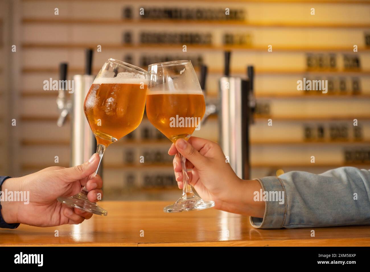 Primo piano di due mani che brucano bicchieri di birra artigianale in un bar moderno. L'atmosfera è calda e accogliente, perfetta per una riunione sociale o di giorno Foto Stock