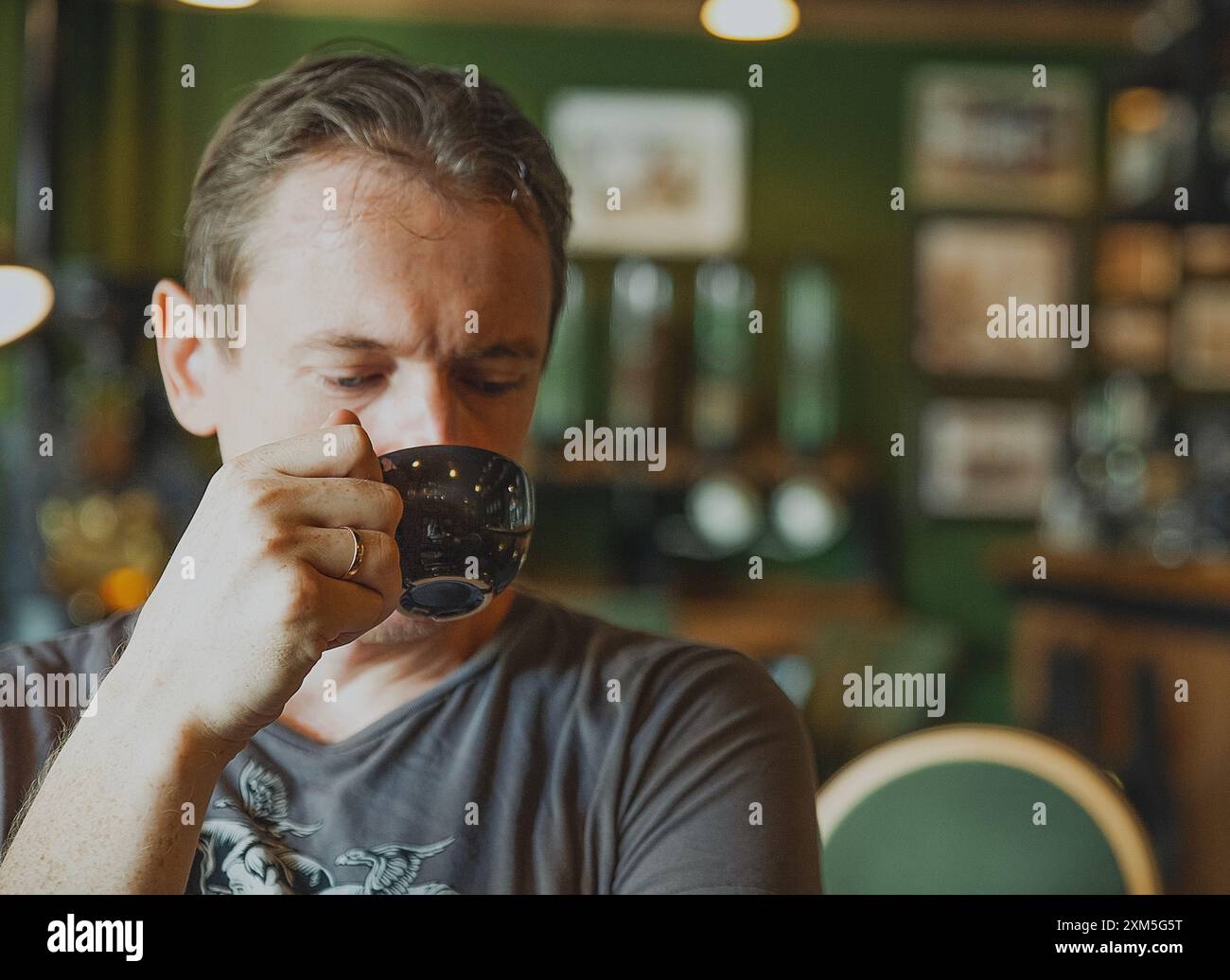 Un uomo nel bellissimo verde interno di un bar beve caffè da una tazza nera Foto Stock