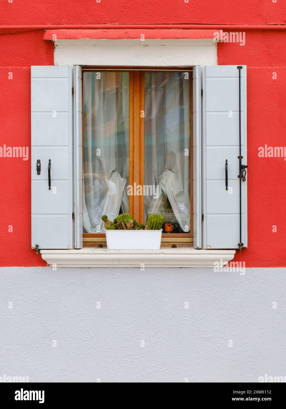 L'intramontabile finestra rossa e bianca si distingue per la sua combinazione di colori classici, che aggiungono un tocco di audacia al paesaggio di Burano Foto Stock