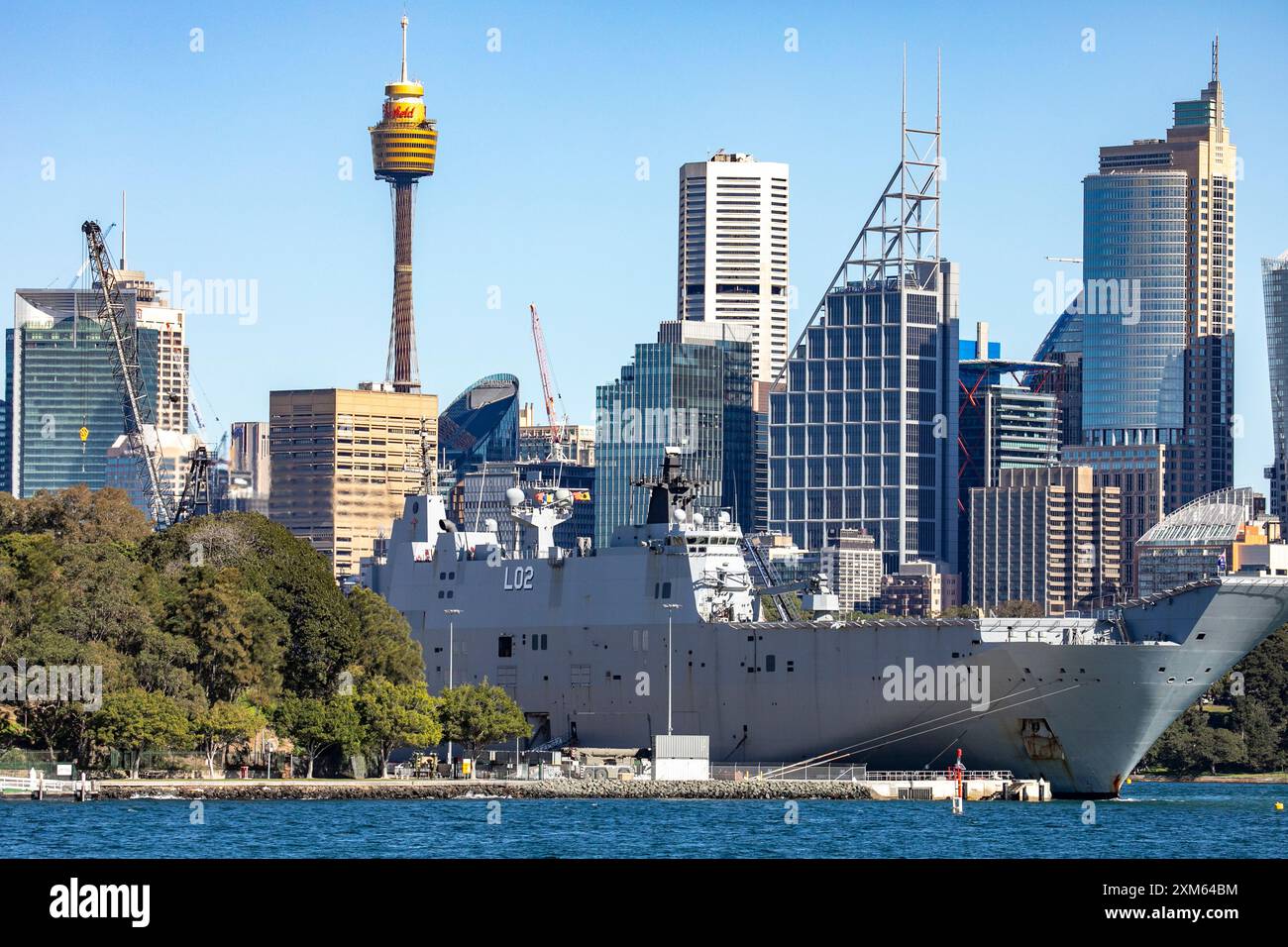 Porto di Sydney, HMAS Canberra nella base navale di Garden Island con la torre di Sydney e i grattacieli del centro città alle spalle, nuovo Galles del Sud, Australia Foto Stock