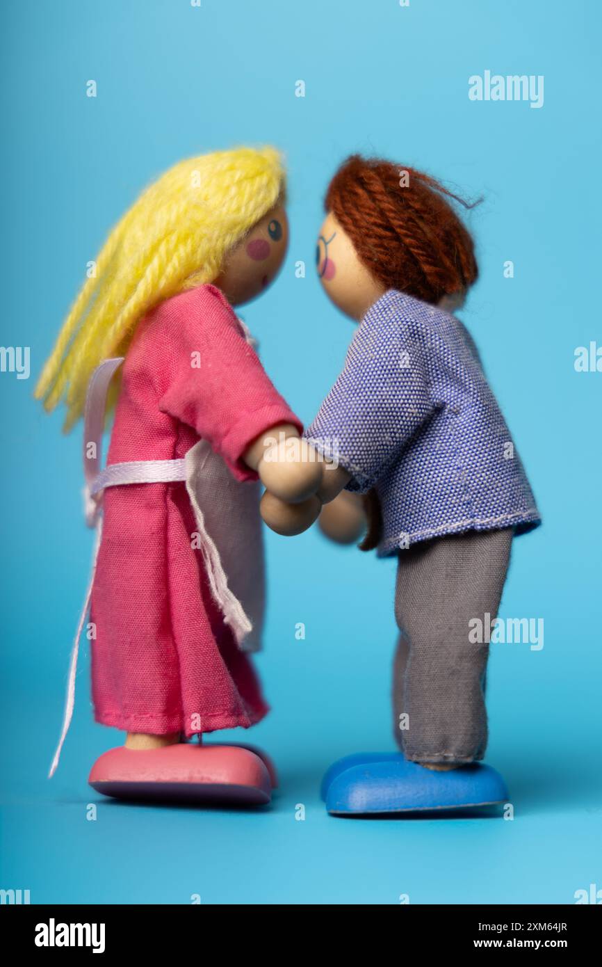 Figure di legno di un uomo e di una donna che si tengono per mano su uno sfondo blu, che rappresentano l'amore e la compagnia eterni. Minimalista ma potente Foto Stock