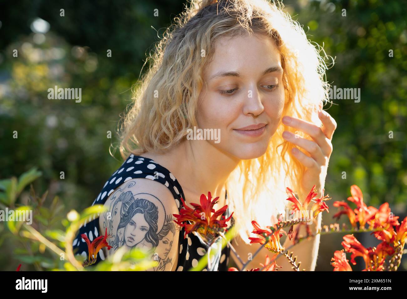 Una donna bionda con tatuaggi sulla spalla ama i fiori in un giardino estivo Foto Stock