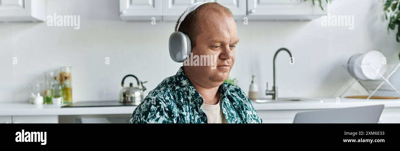 Un uomo con indosso le cuffie lavora su un laptop nella sua cucina. Foto Stock