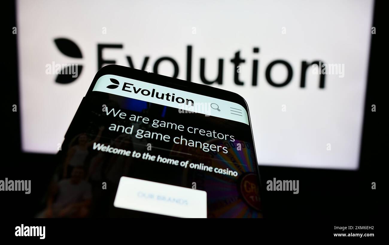 Telefono cellulare con sito web della società svedese di tecnologia del gioco d'azzardo Evolution AB davanti al logo aziendale. Mettere a fuoco in alto a sinistra sul display del telefono. Foto Stock