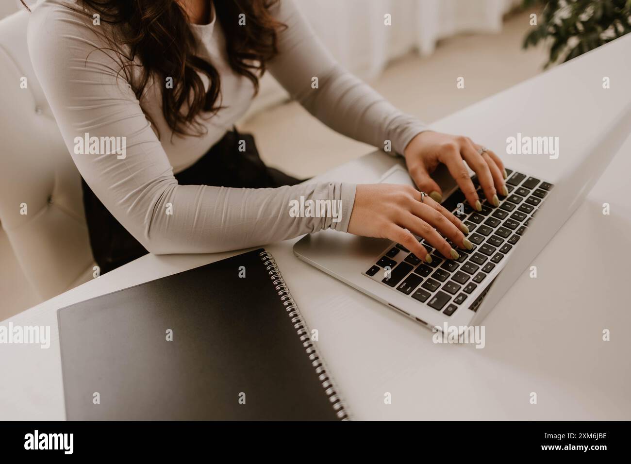 Le mani della giovane donna ispanica scrivono su un notebook, accanto al notebook Foto Stock
