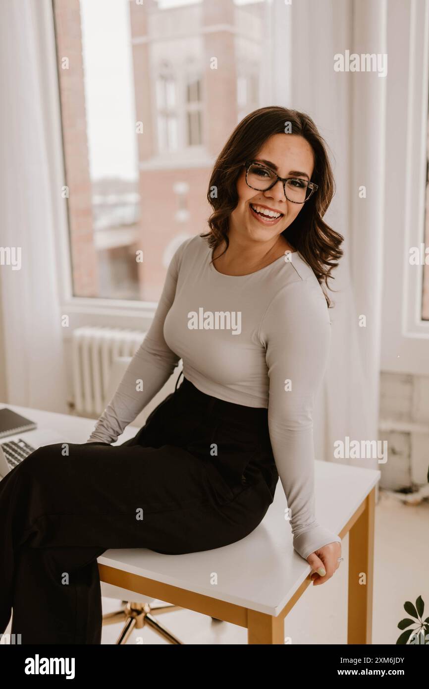 Giovane donna ispanica seduta su una moderna scrivania da ufficio Foto Stock