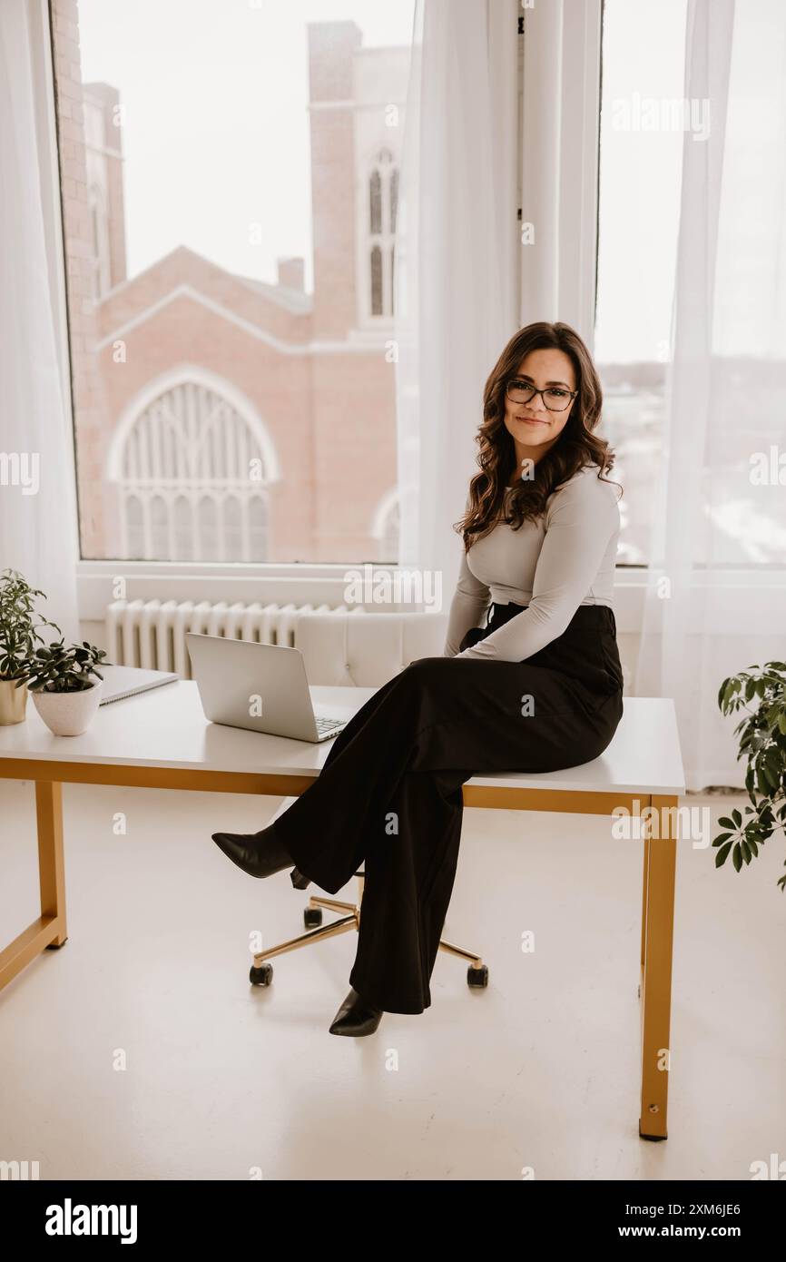 Giovane donna ispanica seduta su una scrivania moderna con un computer portatile Foto Stock