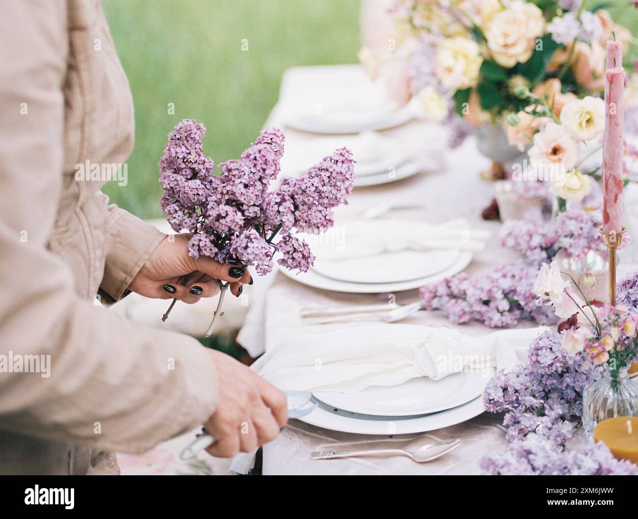 Le mani sistemano fiori lilla su un tavolo all'aperto splendidamente allestito Foto Stock