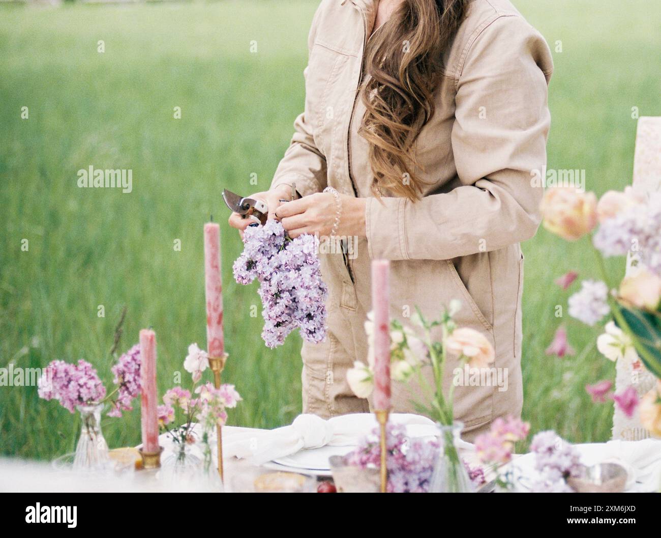 Donna che organizza fiori lilla su un tavolo all'aperto con candele rosa Foto Stock