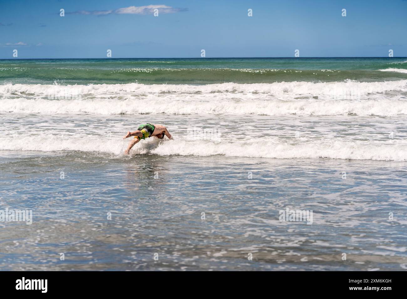 Uomo che si tuffa nelle onde in spiaggia Foto Stock