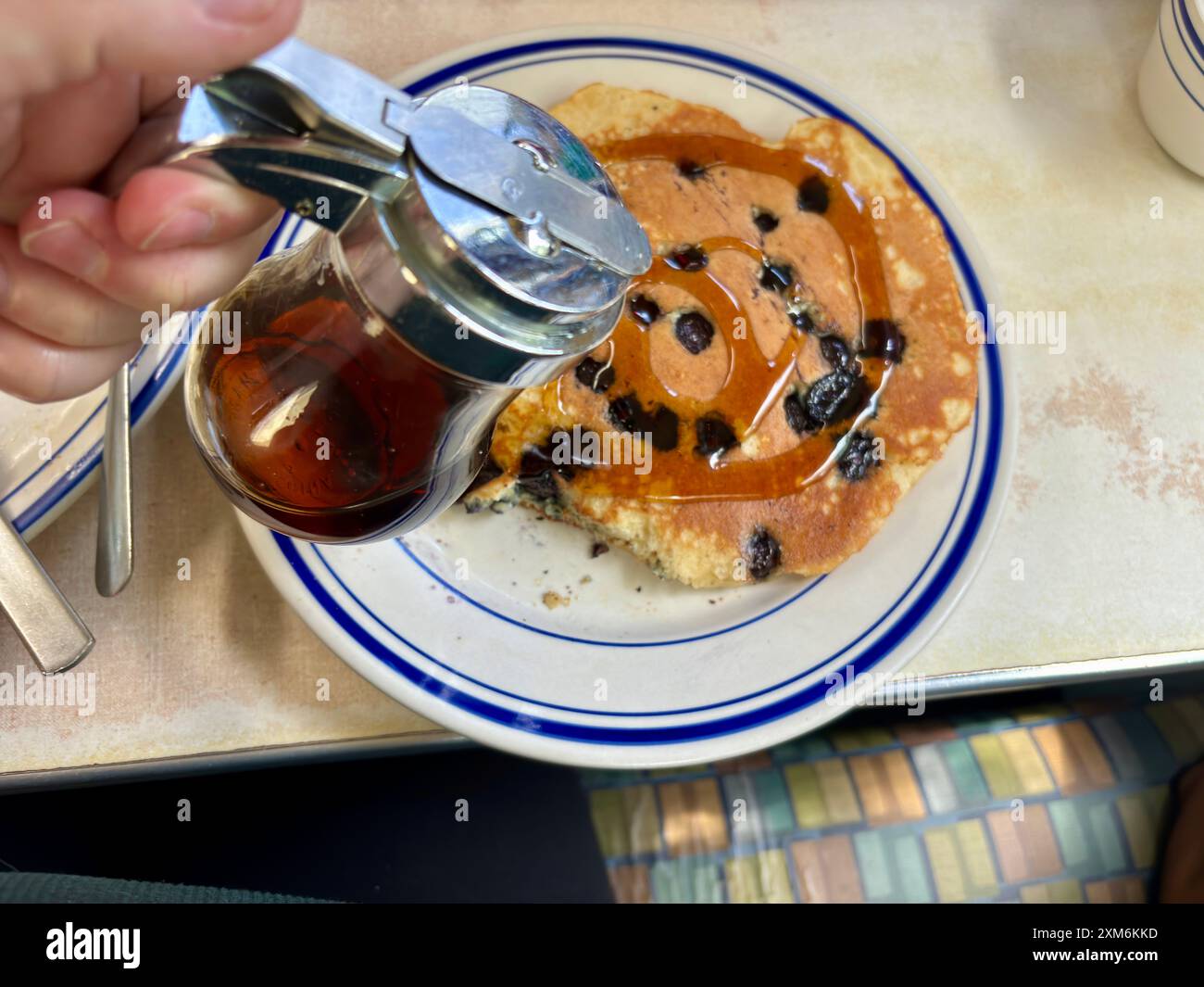 Versare a mano lo sciroppo sul pancake ai mirtilli sul piatto della tavola calda Foto Stock