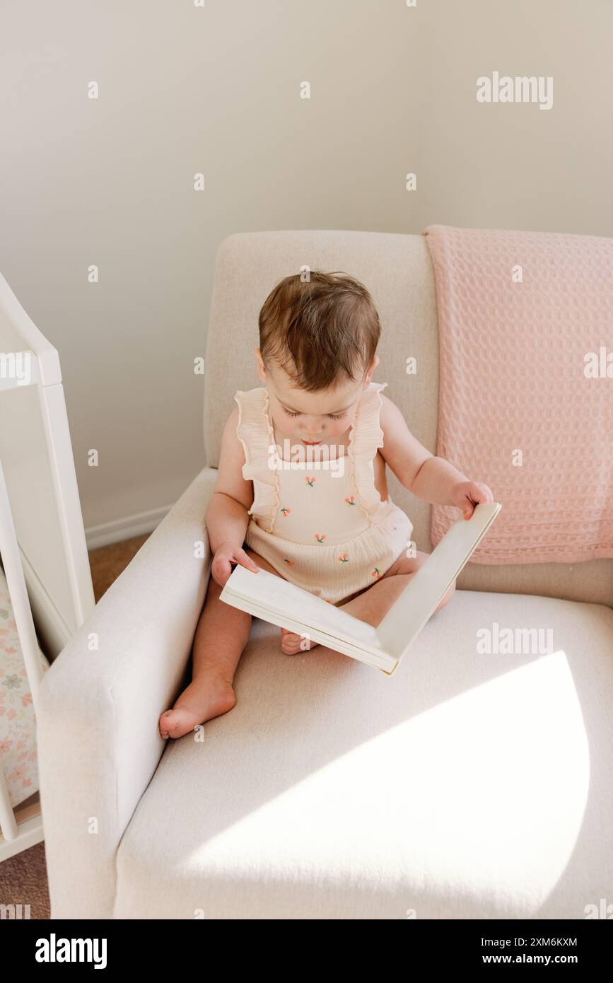 Bambino seduto su una sedia, avvolto in un libro, in un'accogliente nursery Foto Stock