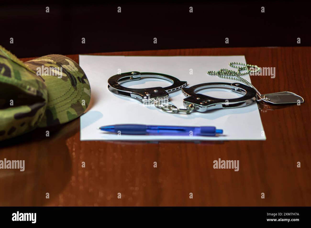 Su un tavolo di legno posare un berretto militare mimetico, un paio di medaglioni dell'esercito, polsini di metallo e una penna blu con un pezzo di carta Foto Stock