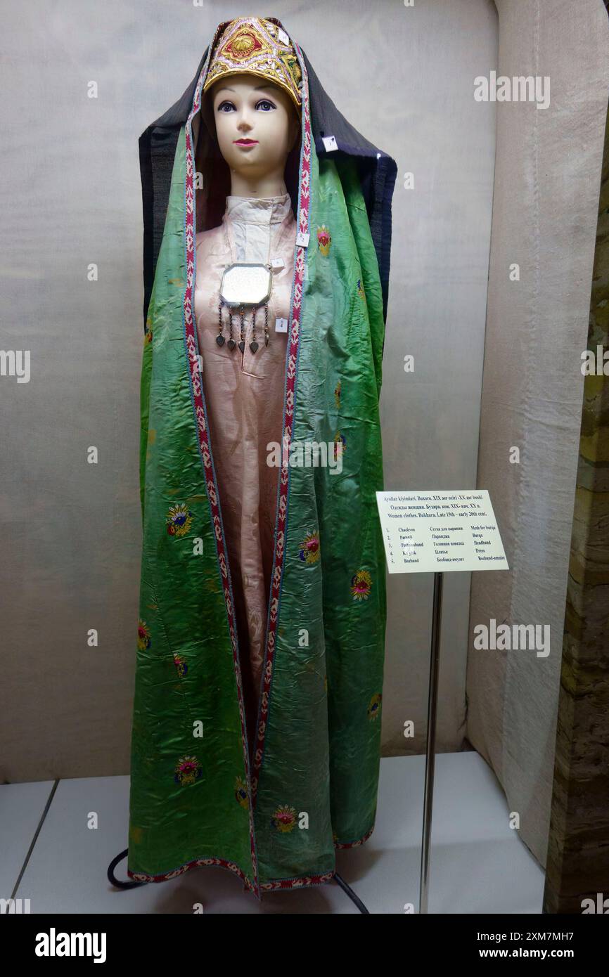 Manichino femminile tradizionale che indossa un colorato costume etnico con mantello ricamato verde e headpiece decorato nel museo di Bukhara, Uzbekistan Foto Stock