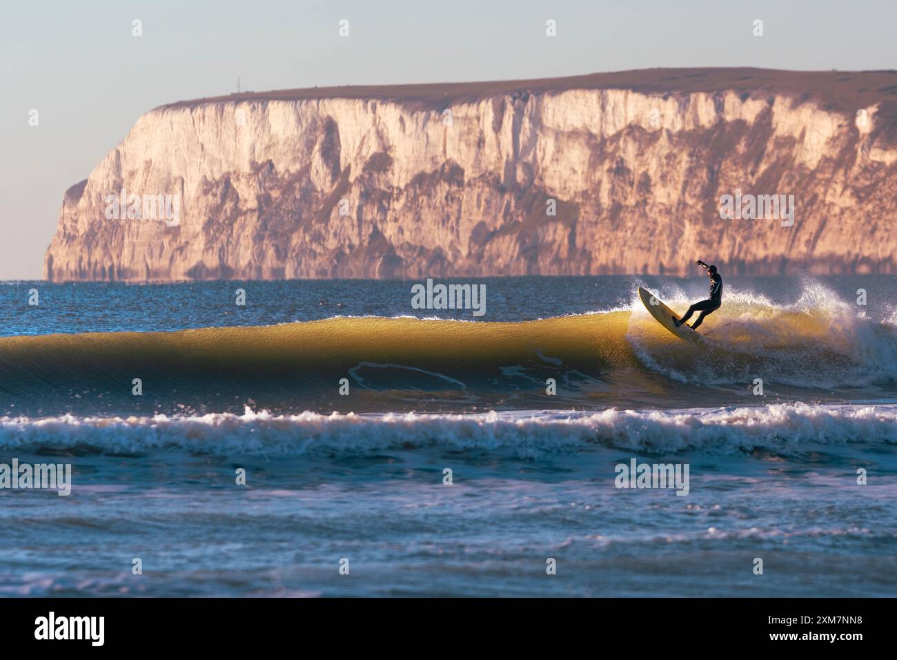 Surfista cavalcando le onde sull'isola di Wight con scogliera e terra sullo sfondo Foto Stock