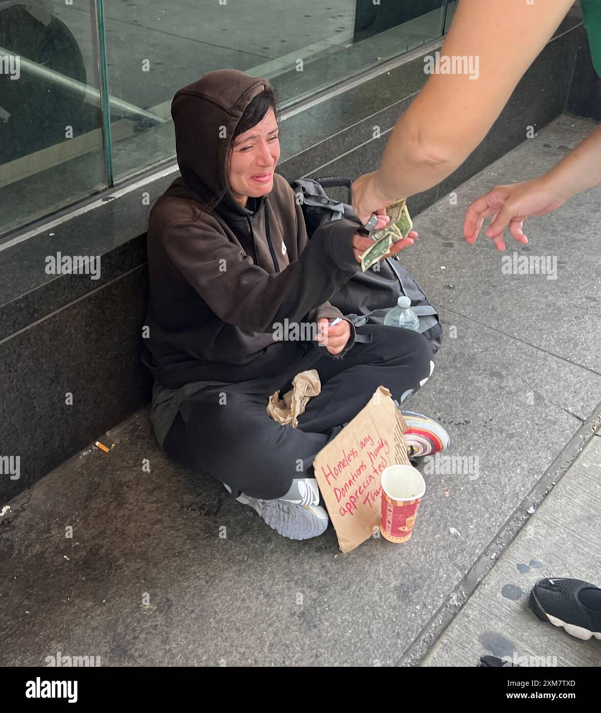 Una senzatetto mostra emozioni grazie a un passante grintoso sulla 5th Avenue nel centro di Manhattan, New York City. Foto Stock