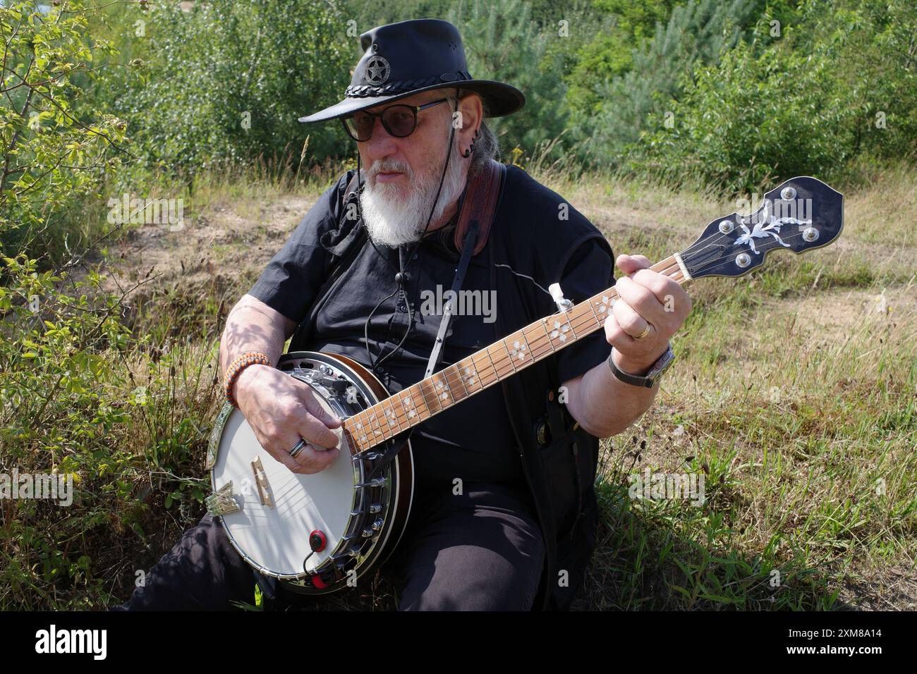 L'uomo anziano con un cappello nero in pelle suona un banjo Foto Stock