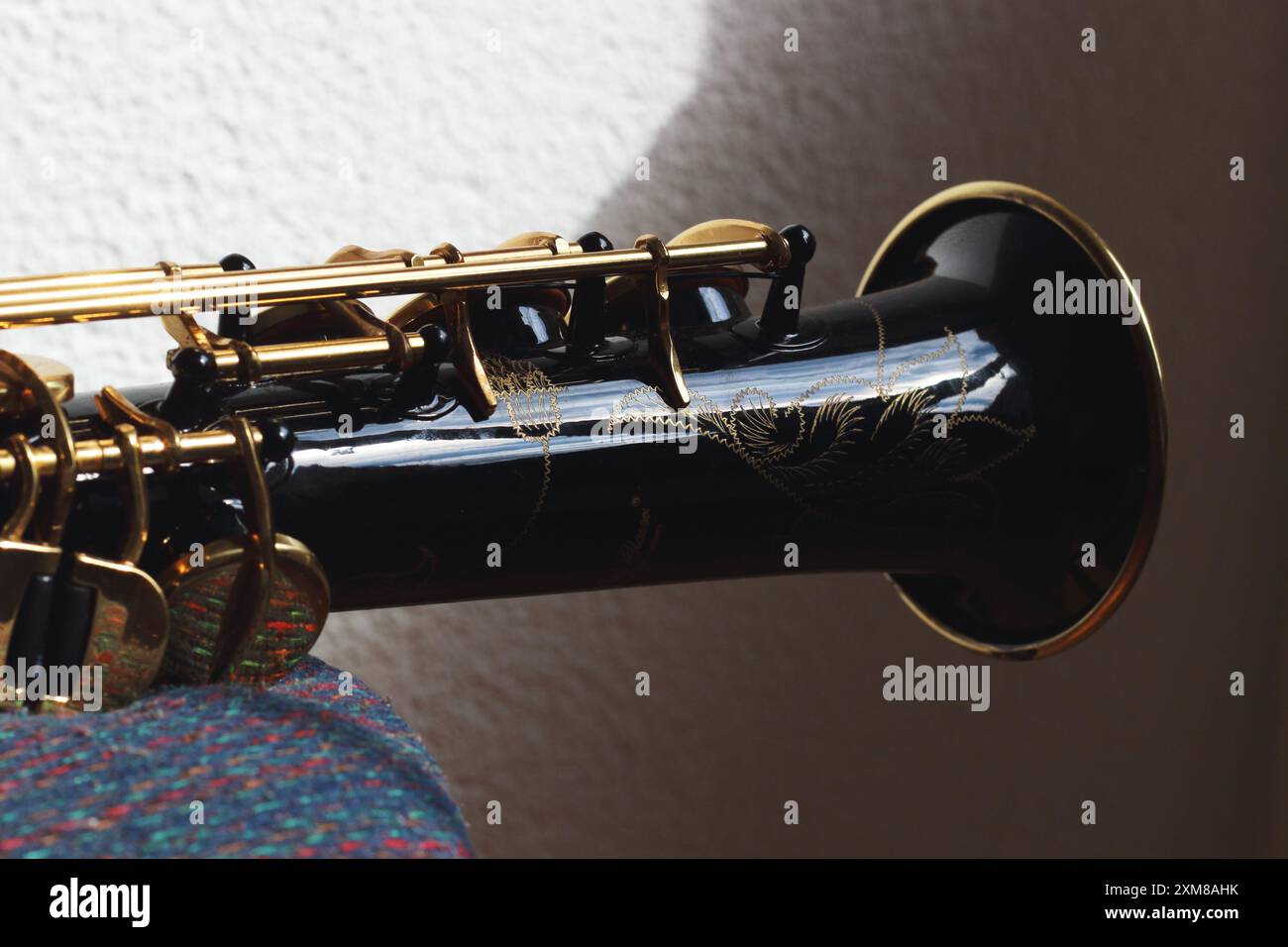 Primo piano della parte a campana di un sassofono dritto di colore nero, che mette in risalto le sue curve morbide e l'intricata maestria artigianale. La superficie lucidata Foto Stock