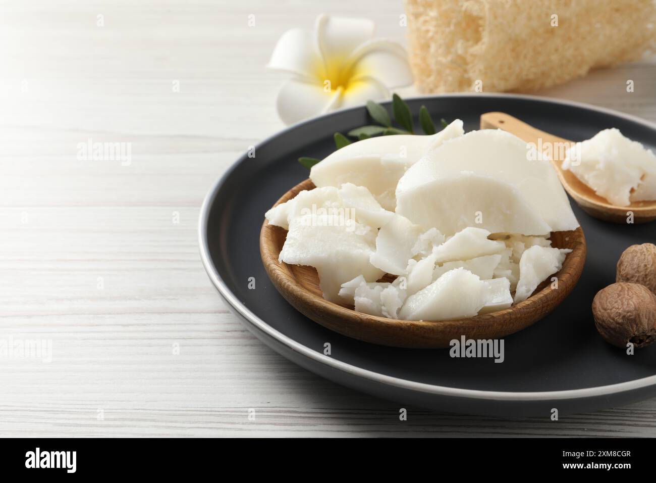 Burro di karité naturale, noci, fiori di plumeria e spugna di loofah su tavolo in legno, spazio per testo Foto Stock