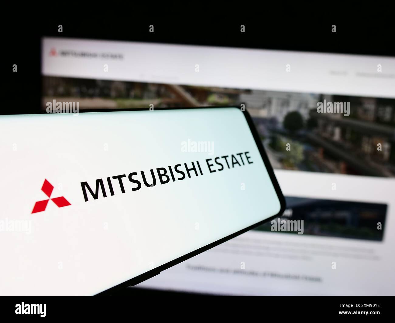 Telefono cellulare con logo della società immobiliare giapponese Mitsubishi Estate Co. Ltd. (MEC) davanti al sito web. Mettere a fuoco la parte centrale sinistra del display del telefono. Foto Stock