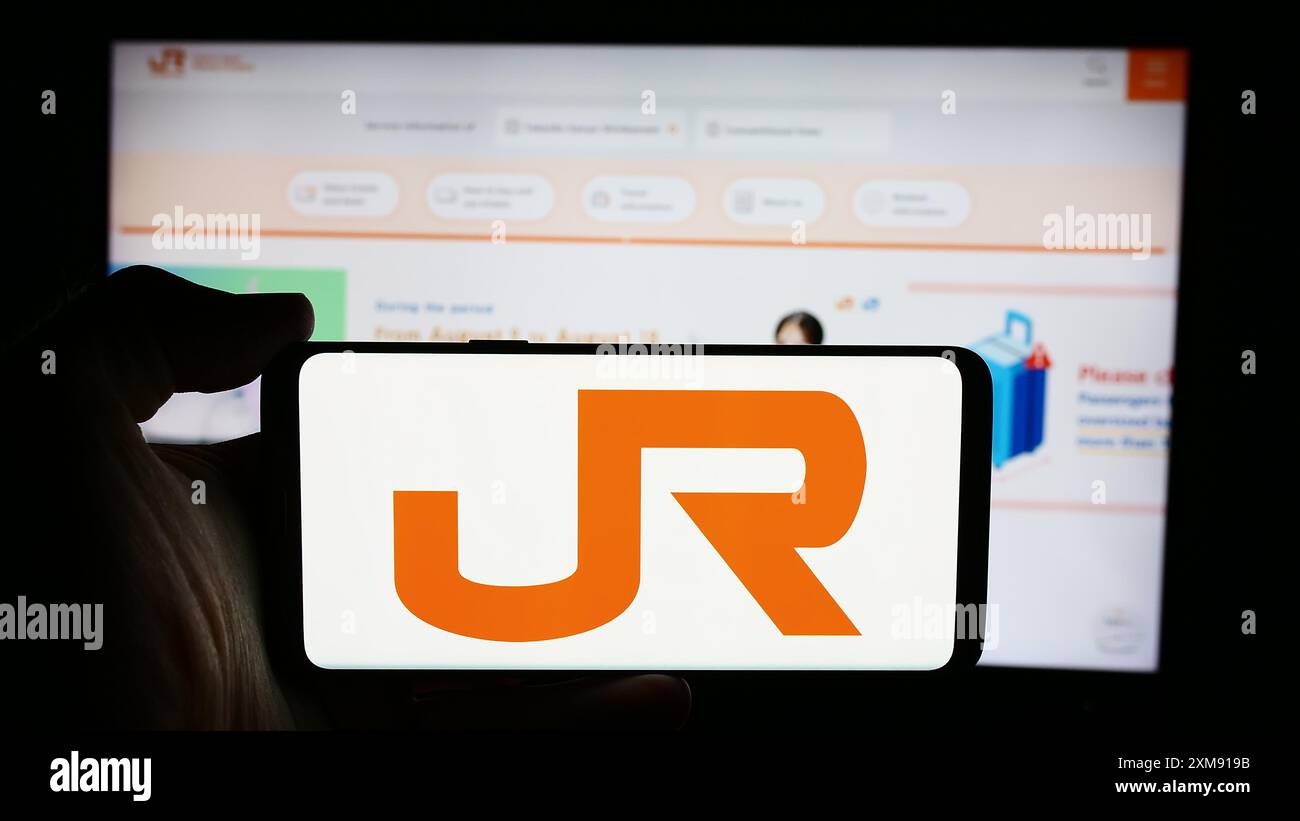 Persona che detiene un cellulare con il logo dell'azienda ferroviaria giapponese Central Japan Railway Company di fronte alla pagina web. Mettere a fuoco il display del telefono. Foto Stock