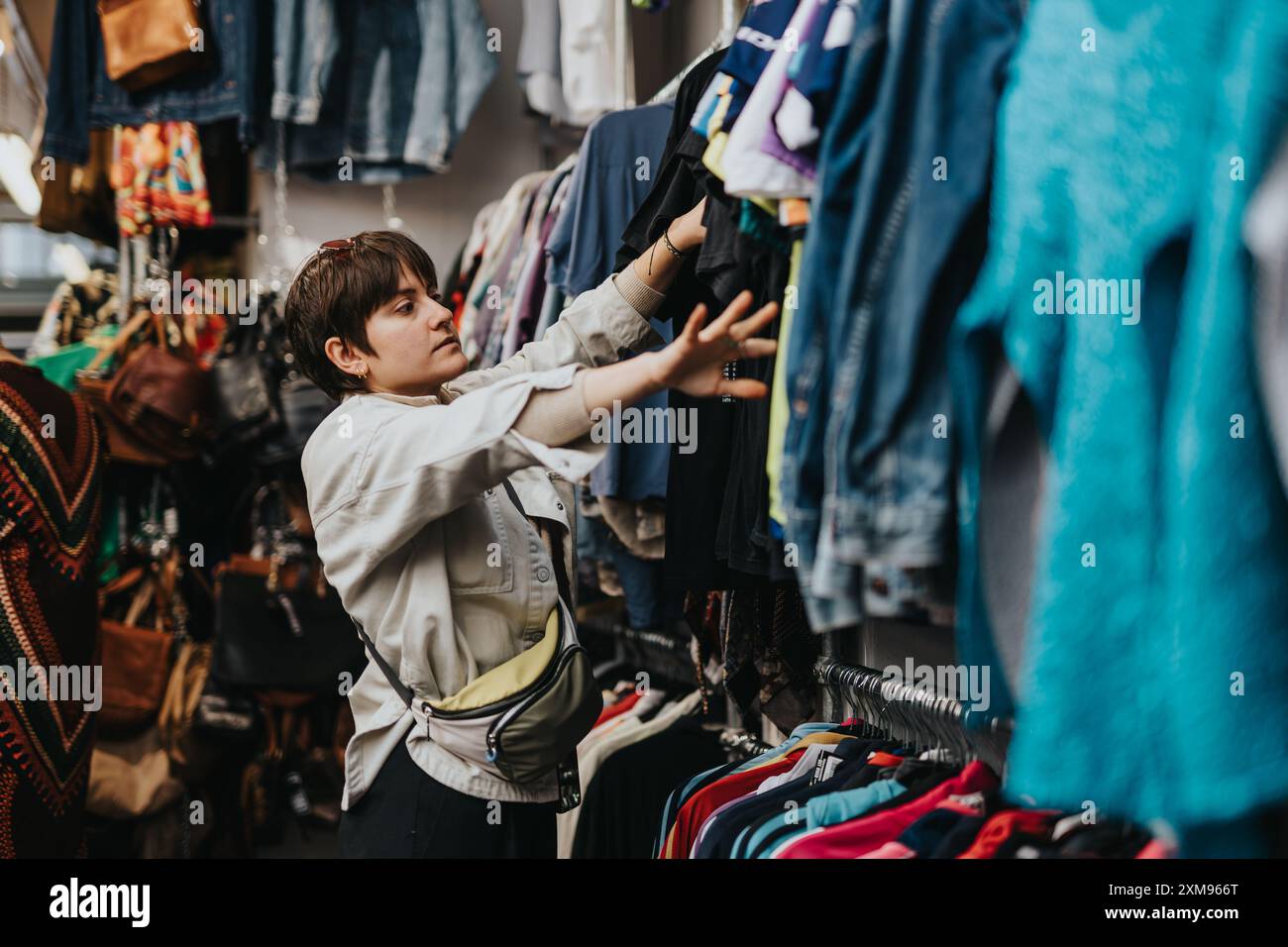 Giovane che sfoglia i vestiti in un negozio di articoli di seconda mano mentre acquista capi di abbigliamento di seconda mano Foto Stock