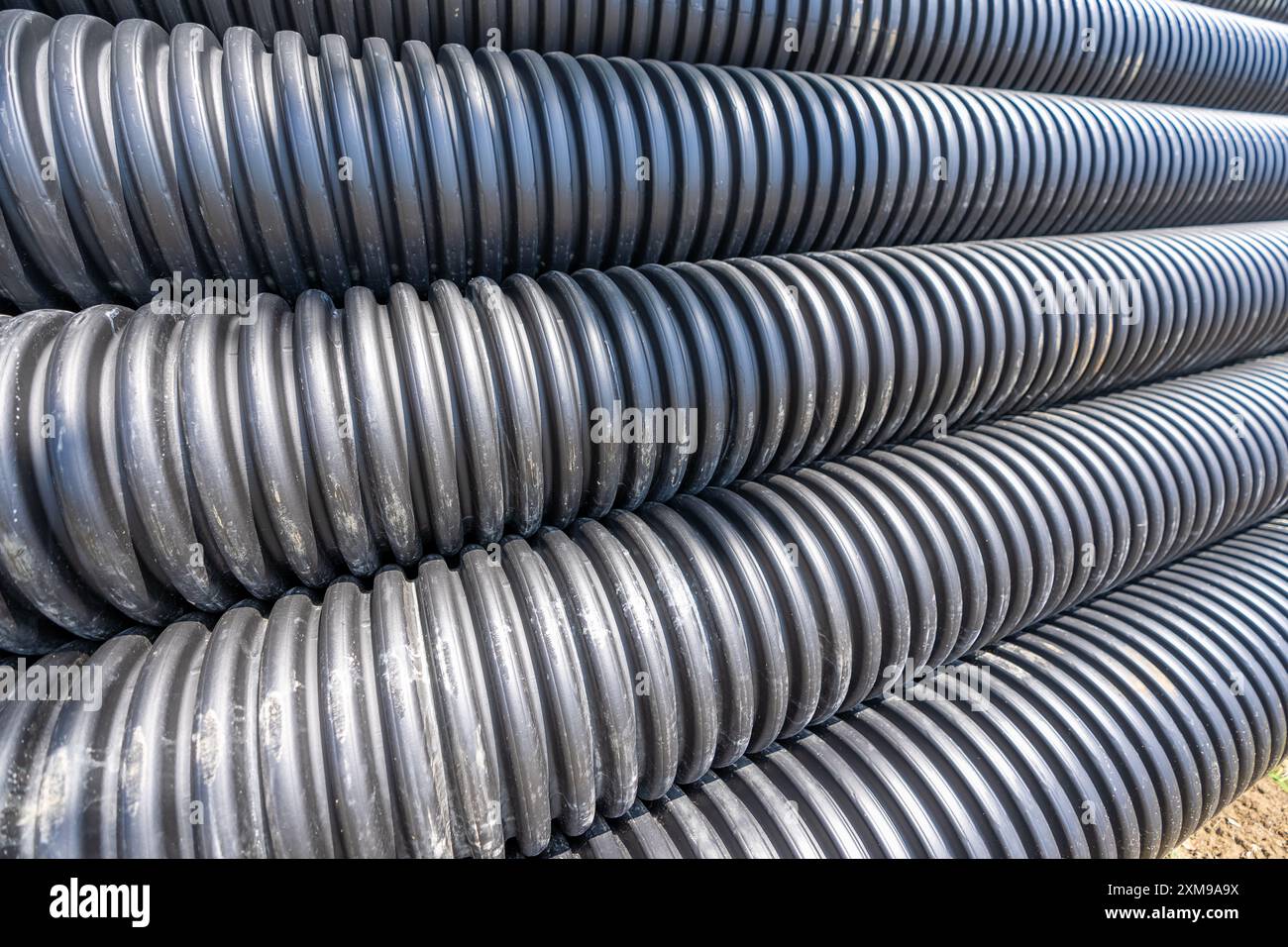 Pila di tubi fognari in HDPE nero (plastica in HDPE N-12) in un sito di progetto in attesa di installazione. Foto Stock