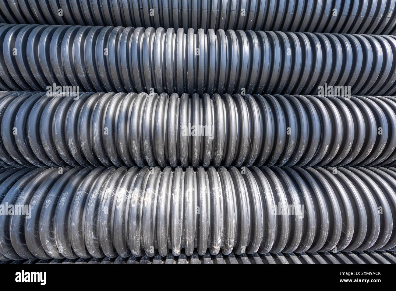 Pila di tubi fognari in HDPE nero (plastica in HDPE N-12) in un sito di progetto in attesa di installazione. Foto Stock