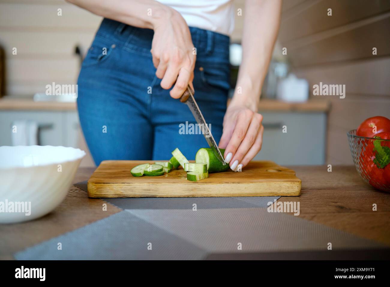 Vista ravvicinata di una donna che taglia cetrioli freschi su un tagliere di legno Foto Stock