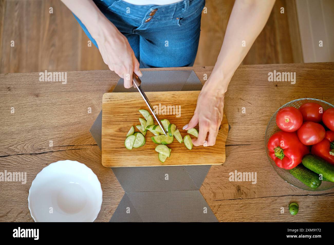 Vista dall'alto delle mani femminili che affettano cetriolo fresco su un tagliere di legno Foto Stock
