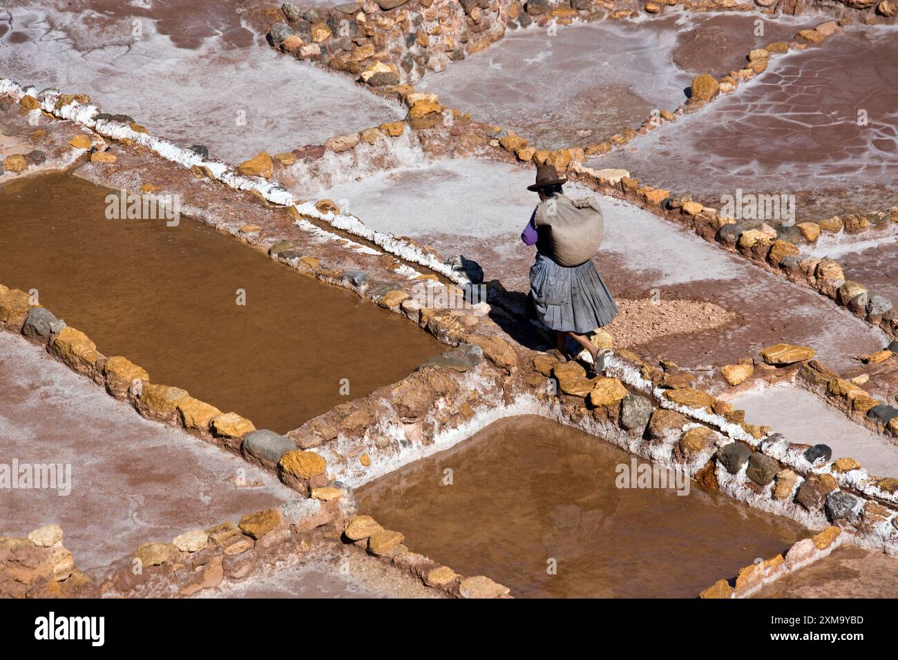 Donna locale che lavora nelle miniere di sale di Maras, situate su una montagna sopra Urubamba in Perù. Le miniere di sale sono costituite da numerose piscine poco profonde riempite di acqua salata. Quando l'acqua evapora, lascia sale cristallizzato. Queste saline sono in uso da oltre 500 anni e sono ancora gestite da famiglie locali per estrarre sale rosa peruviano. Foto Stock