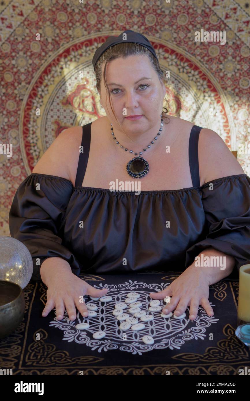 Un indovino zingaro vestito di nero predice il futuro con pietre rune Foto Stock