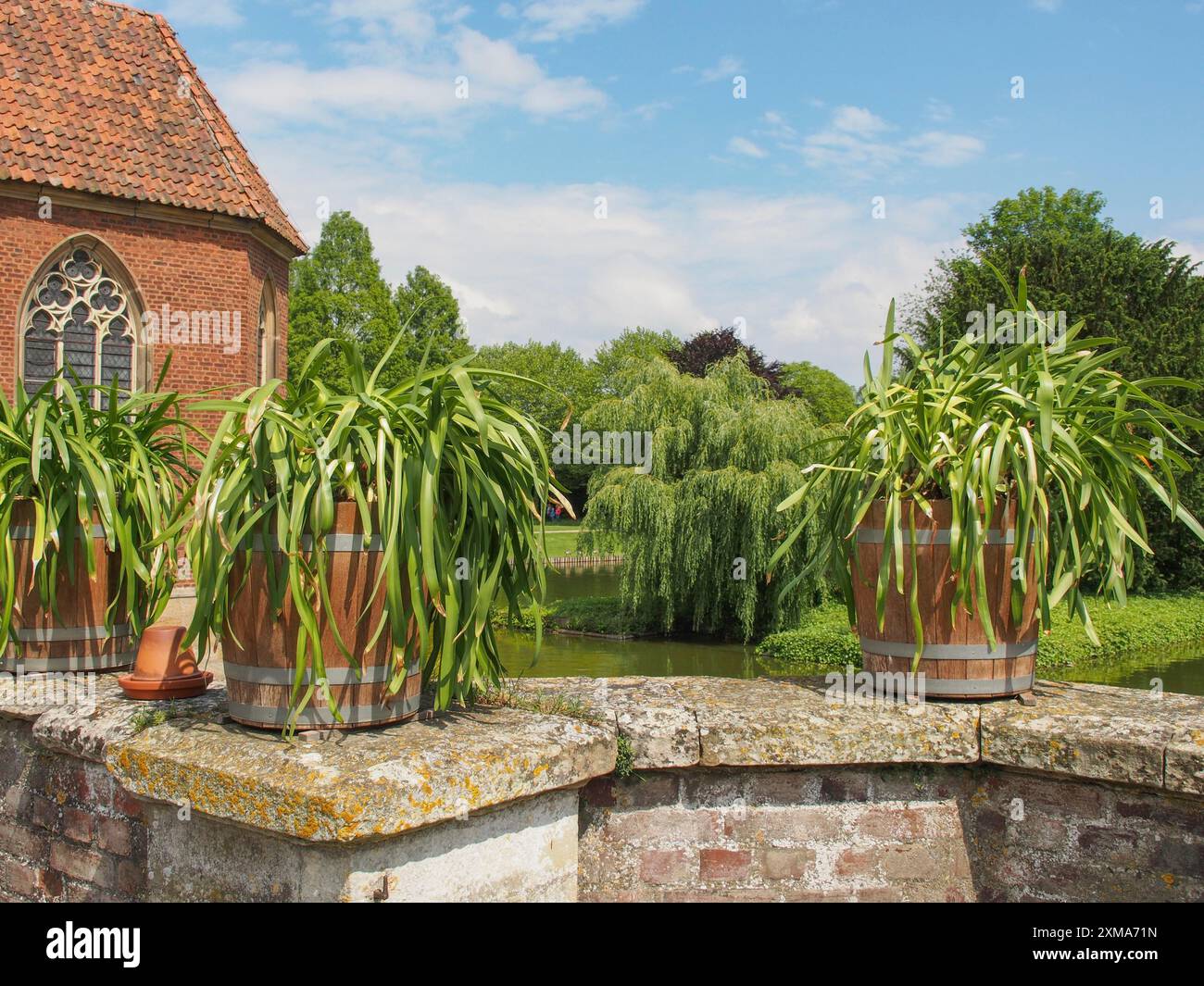 Vasi di fiori su un muro di mattoni di fronte a un edificio storico con finestra gotica e sfondo verde, Havixebeck, muensterland, germania Foto Stock