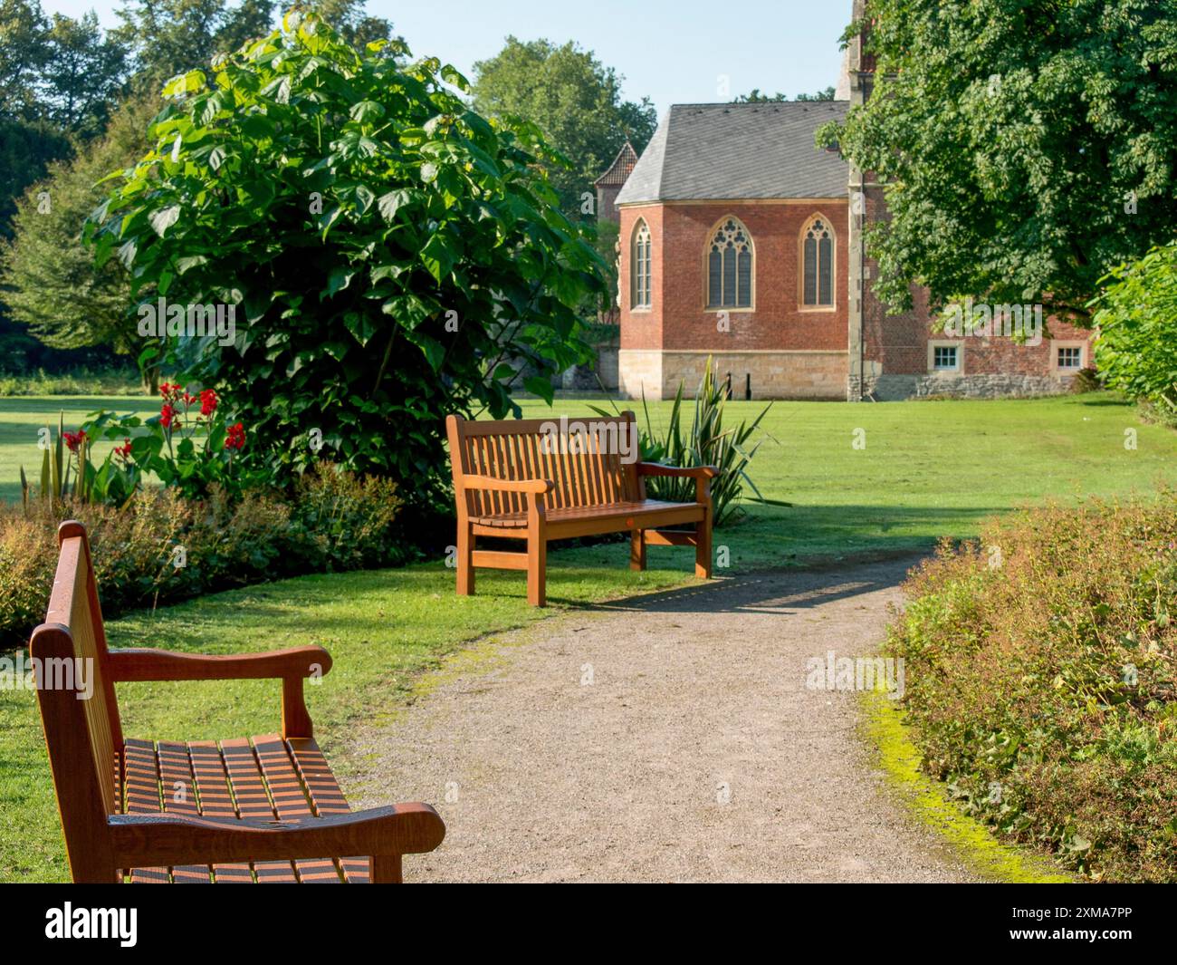 Panchine in legno lungo un sentiero con una chiesa sullo sfondo, havixbeck, germania Foto Stock