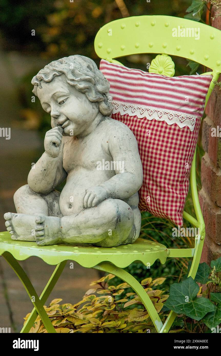 Scultura in pietra per bambini su una sedia verde con cuscino rosso e bianco nel giardino, borken, vestfalia, germania Foto Stock