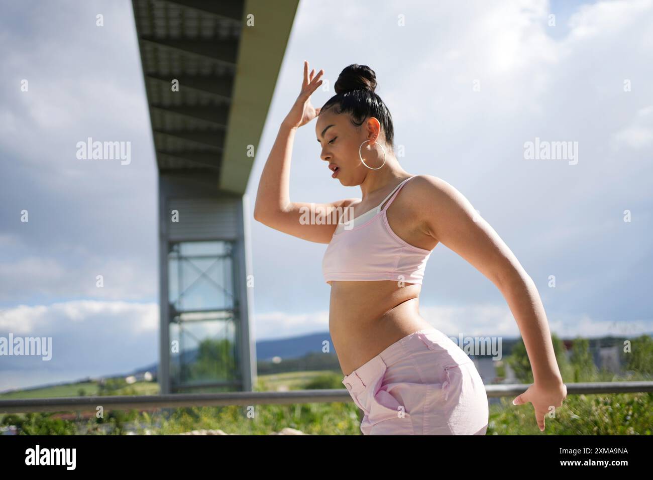 Una donna sta ballando di fronte a un ponte. Indossa una canotta rosa e pantaloncini rosa Foto Stock Una donna sta ballando di fronte a un ponte. Indossa una canotta rosa e pantaloncini rosa Foto Stock