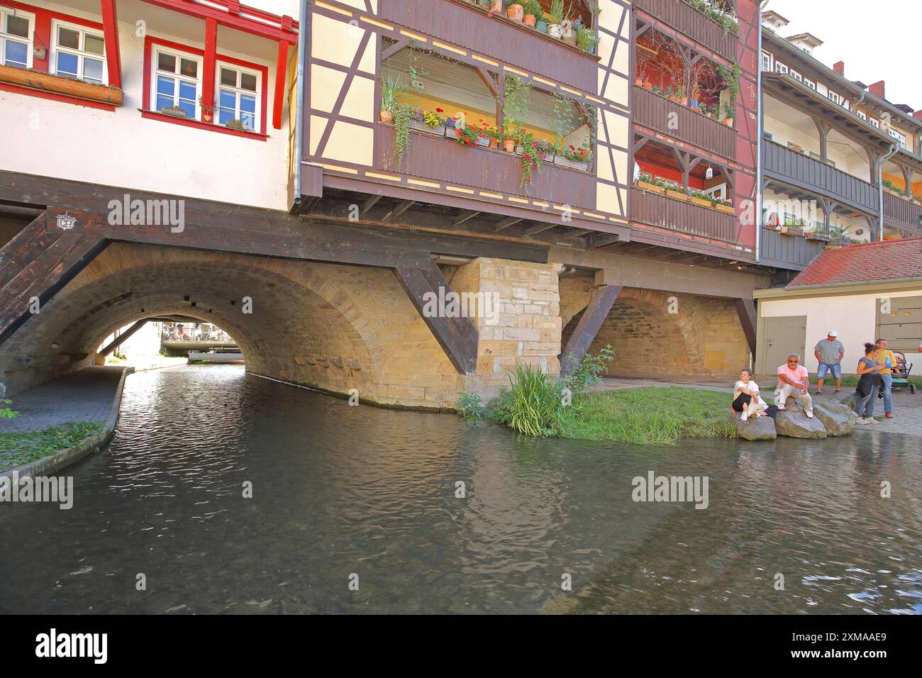 Famosa Kraemerbruecke con il fiume Gera e persone sedute sulla riva, idilliaco, case a graticcio, case a ponte, Erfurt, Turingia, Germania Foto Stock