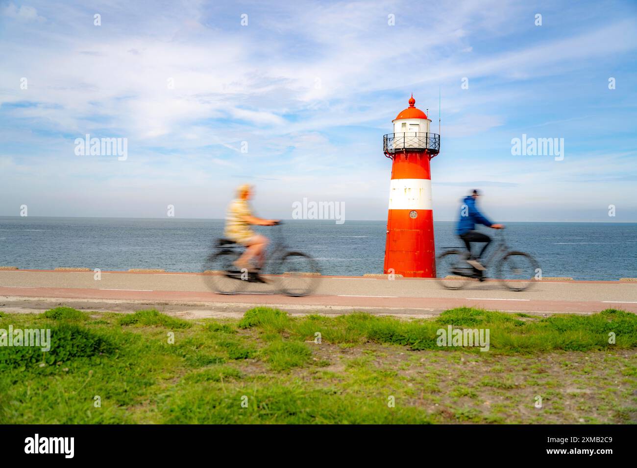 Diga del Mare del Nord vicino a Westkapelle, faro di Westkapelle Laag, ciclisti sulla pista ciclabile Zeeuwse Wind Route, provincia della Zelanda, Walcheren Foto Stock