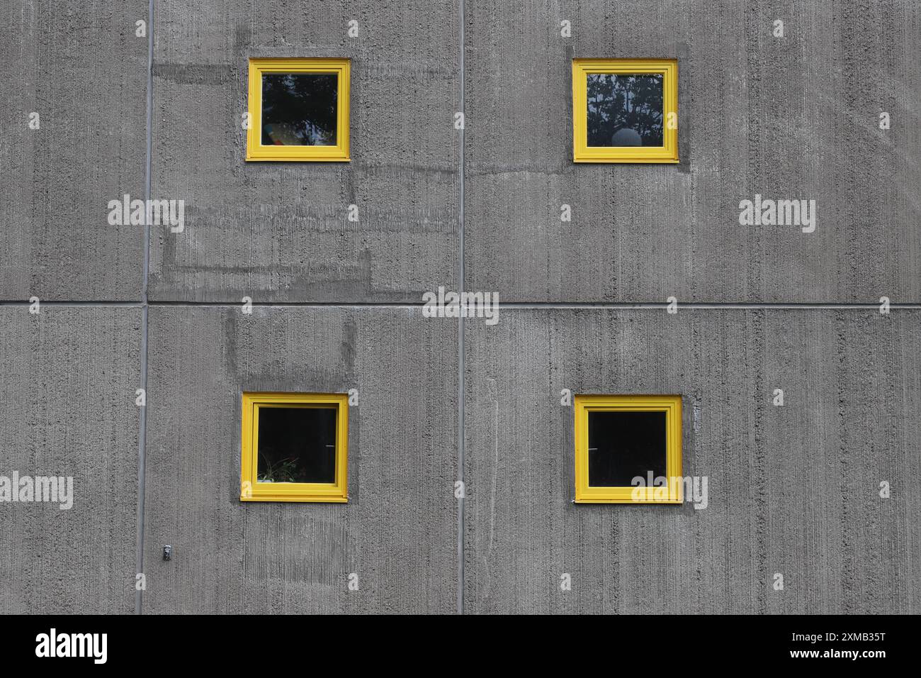 Quattro piccole finestre incorniciate in giallo in un muro di cemento. Foto Stock