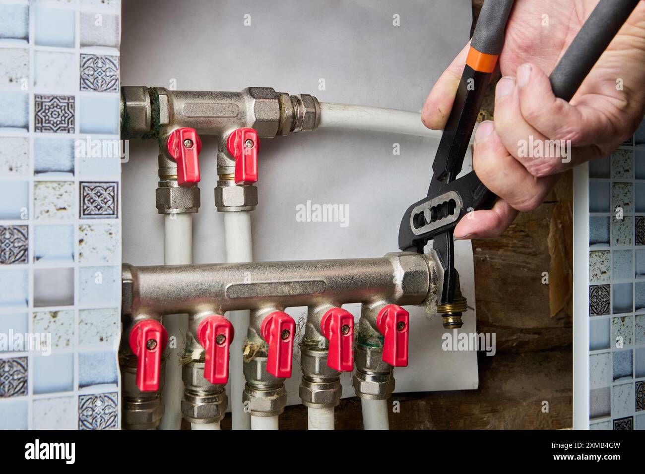 Per la riparazione del collettore del tubo dell'acqua in una casa di campagna, l'idraulico utilizza pinze regolabili per svitare il raccordo a gomito. Foto Stock