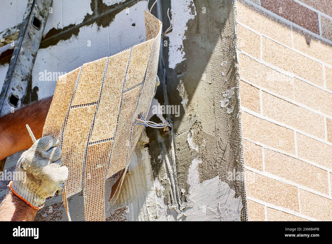 Installando l'impiallacciatura di mattoni all'esterno, l'operaio decora la facciata della casa con un pannello esterno di finti mattoni sottili. Foto Stock