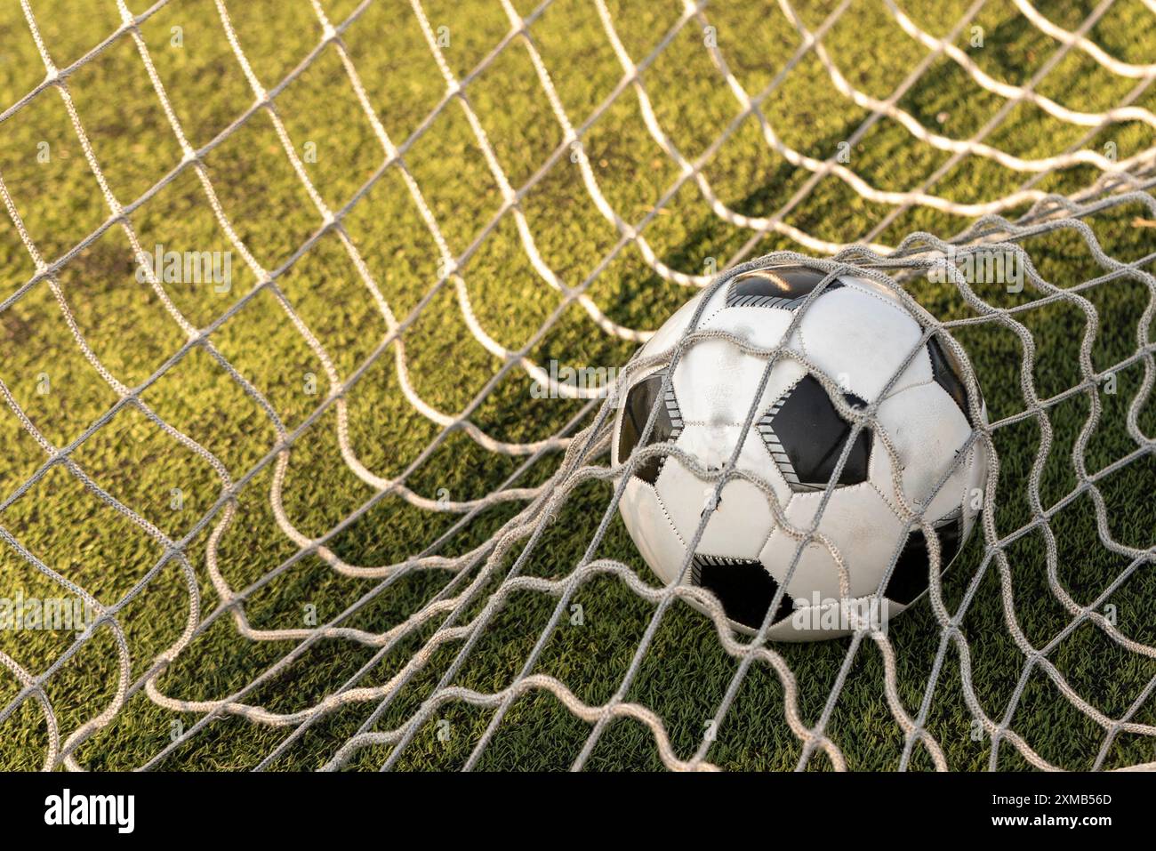 Un pallone da calcio bianco e nero spinto da un colpo potente, che si strappa attraverso la rete in un gol perfetto. La rete rigonfiante sottolinea l'impatto e la prec Foto Stock