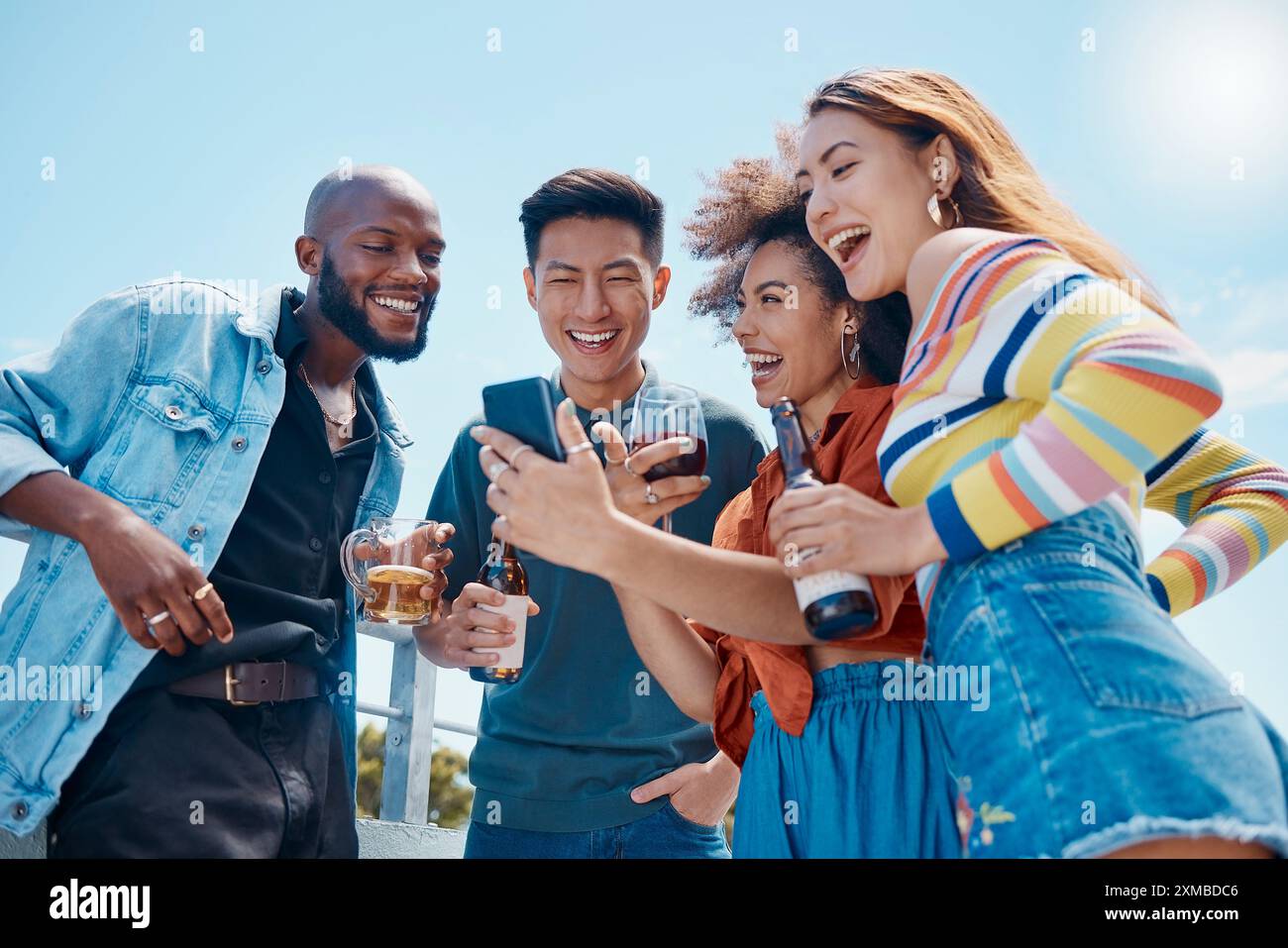 Smartphone, diversità e bevande con gli amici in vacanza, ridendo insieme a meme durante il weekend. Sorridi, gruppo felice e gente multirazziale Foto Stock